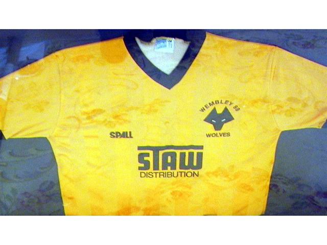 459. Shirt: An old gold with black trim V-neck shirt, Wolverhampton Wanderers crest to front with ‘Wembley 88’ above and sponsors ‘Staw Distribution’ below. Mounted, framed and glazed. Illus. £500-600